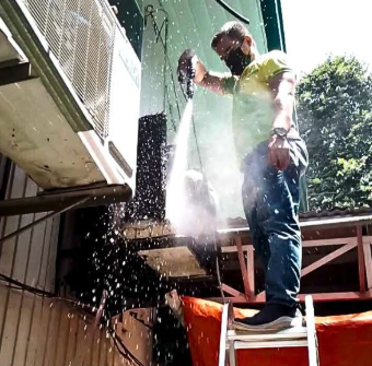 PrimeChem technician pressure-washing an outdoor AC condenser unit